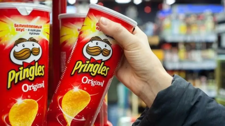 Человек хватает банку Pringles с полки Человек хватает банку Pringles с полки