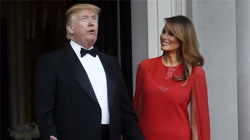 Мелания Трамп в красном платье улыбается во время разговора Дональда Трампа