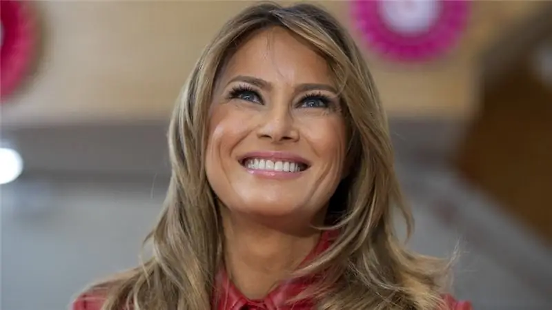 Мелания Трамп в красной куртке улыбается, глядя вверх